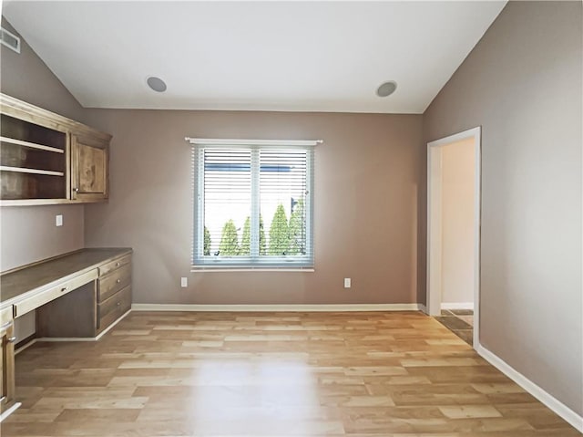 interior space with light wood finished floors, built in study area, baseboards, and vaulted ceiling