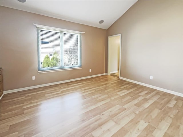 empty room with light wood-style flooring, baseboards, and lofted ceiling