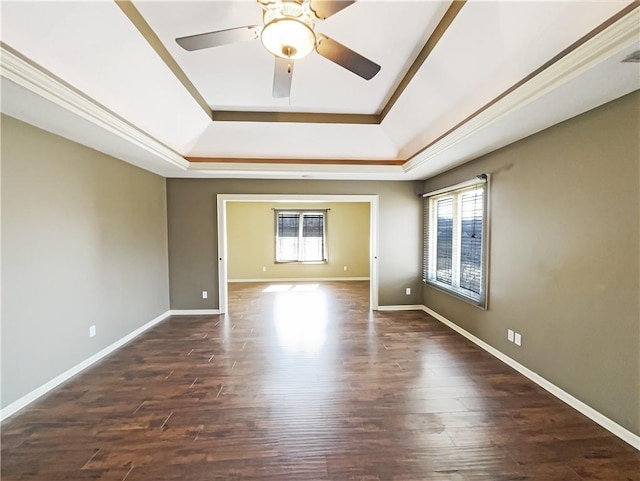 empty room featuring a tray ceiling, baseboards, and dark wood-type flooring