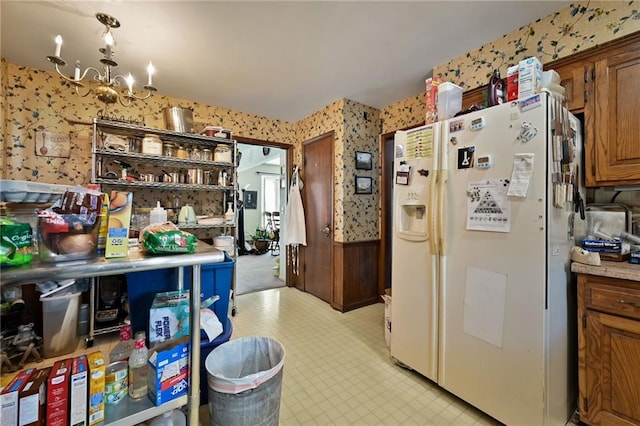 kitchen featuring light floors, wallpapered walls, white fridge with ice dispenser, a notable chandelier, and brown cabinets