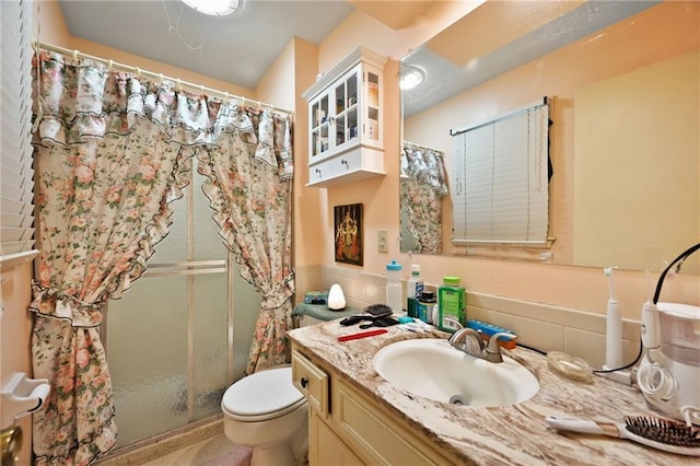 full bathroom with a shower stall, vanity, tile walls, and toilet