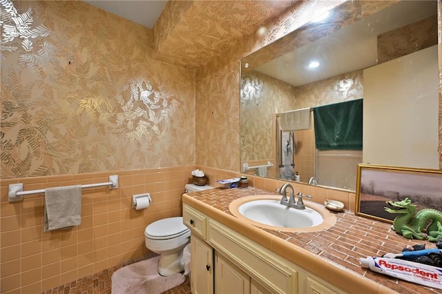 full bathroom featuring wallpapered walls, toilet, vanity, and wainscoting