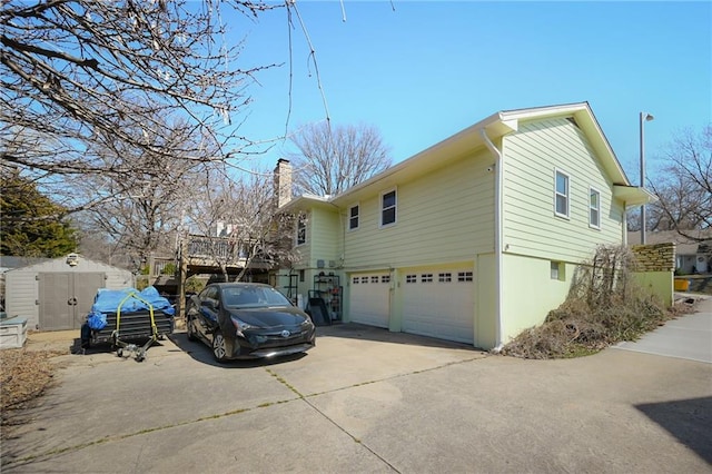 view of home's exterior featuring a shed, an outdoor structure, concrete driveway, an attached garage, and a chimney