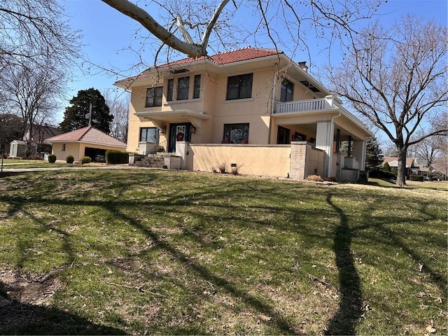 view of front of home featuring a balcony, stucco siding, a tile roof, and a front yard