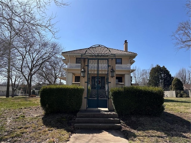 view of front of house featuring stucco siding, a balcony, fence, and a chimney