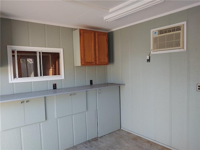 kitchen with an AC wall unit, concrete flooring, light countertops, brown cabinets, and a decorative wall