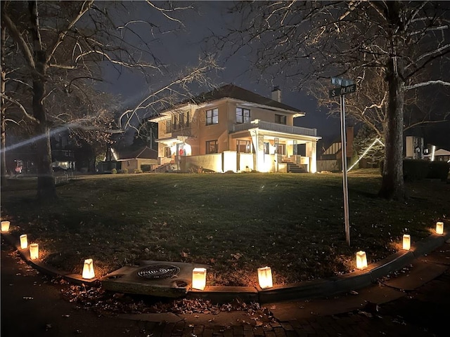 back of house at night with a lawn and a chimney