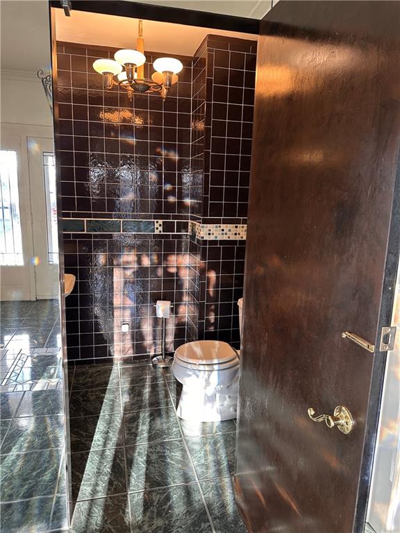 bathroom featuring tile patterned floors, toilet, ornamental molding, tile walls, and a chandelier