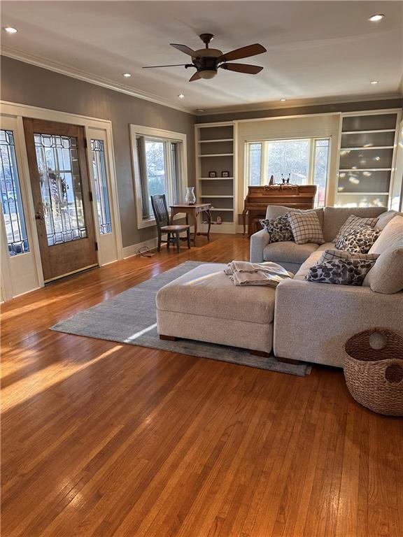 living area featuring hardwood / wood-style floors, built in shelves, a ceiling fan, recessed lighting, and crown molding