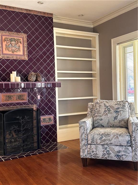 living area with dark wood-style flooring, built in shelves, an accent wall, and ornamental molding