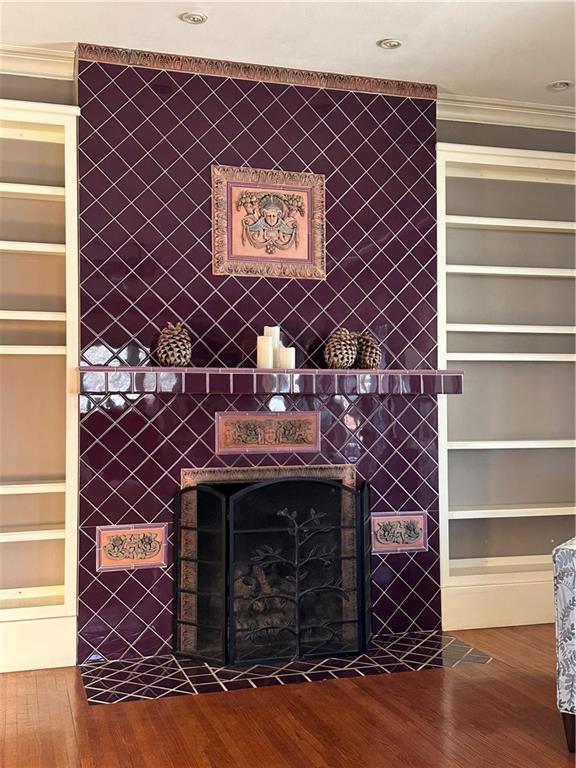 details featuring built in shelves, a fireplace, wood finished floors, and crown molding