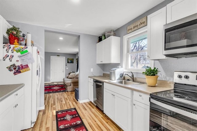 kitchen featuring light wood finished floors, light countertops, white cabinets, stainless steel appliances, and a sink