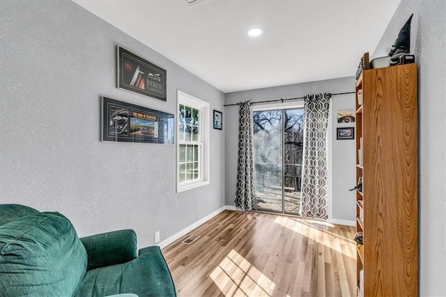 sitting room featuring visible vents, baseboards, wood finished floors, and a textured wall