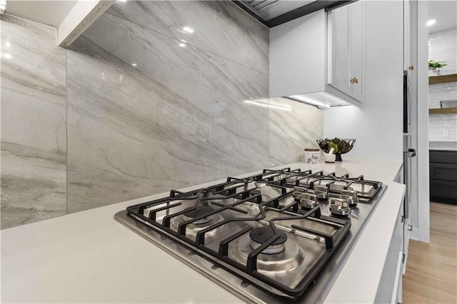 interior details featuring stainless steel gas cooktop, decorative backsplash, light wood-type flooring, and light countertops