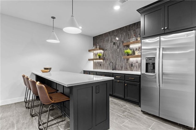 kitchen featuring a breakfast bar area, open shelves, decorative backsplash, light countertops, and stainless steel refrigerator with ice dispenser