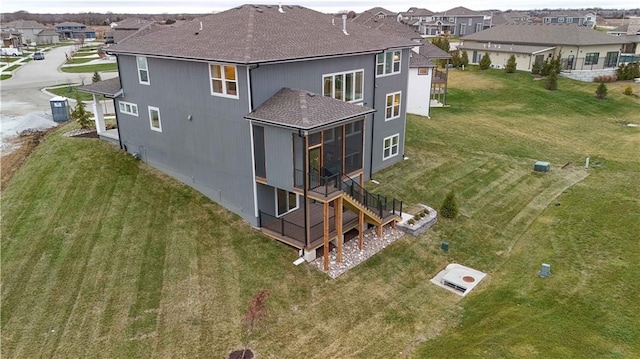 rear view of property featuring a yard, a residential view, a sunroom, and roof with shingles