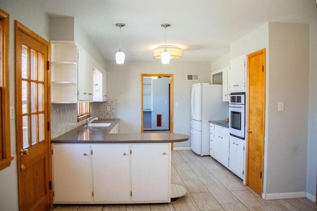 kitchen with open shelves, a peninsula, freestanding refrigerator, a sink, and wall oven