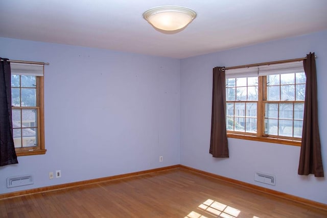 spare room featuring a wealth of natural light, baseboards, and wood finished floors