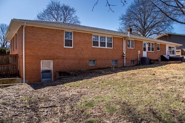 rear view of property with brick siding, cooling unit, and fence