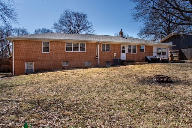 back of house with brick siding, a lawn, a chimney, and central AC