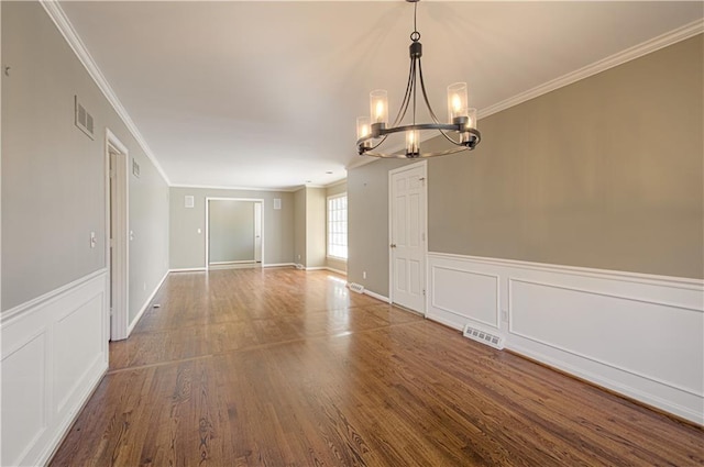 empty room with an inviting chandelier, wood finished floors, visible vents, and ornamental molding