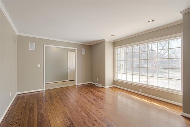 empty room featuring crown molding, wood finished floors, baseboards, and visible vents