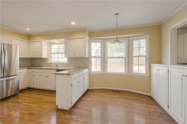 kitchen with wood finished floors, freestanding refrigerator, white cabinets, crown molding, and tasteful backsplash