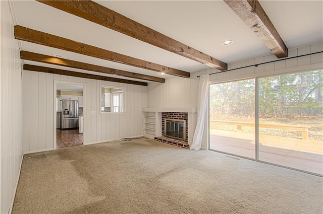 unfurnished living room featuring a wealth of natural light, beamed ceiling, carpet, and a fireplace