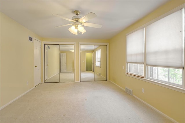 unfurnished bedroom featuring carpet flooring, baseboards, visible vents, and two closets