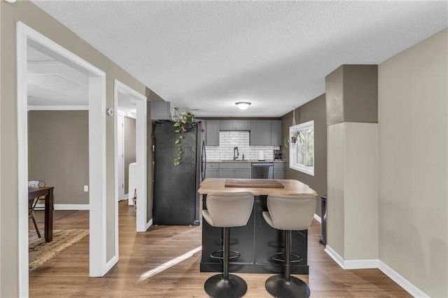 kitchen featuring gray cabinetry, stainless steel dishwasher, wood finished floors, freestanding refrigerator, and light countertops