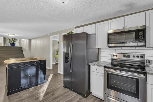 kitchen with decorative backsplash, stainless steel appliances, wood finished floors, a textured ceiling, and white cabinetry