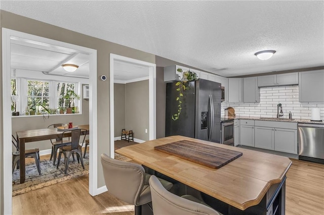 kitchen featuring light wood finished floors, a sink, stainless steel appliances, a textured ceiling, and backsplash