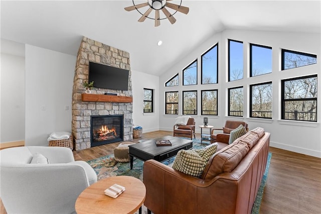 living room with baseboards, high vaulted ceiling, a stone fireplace, and wood finished floors