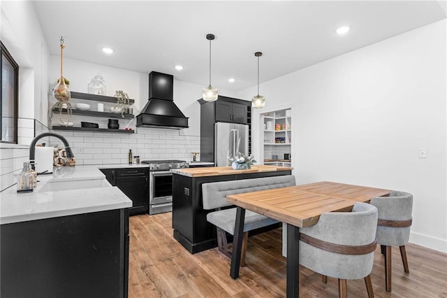 kitchen with open shelves, dark cabinetry, custom exhaust hood, stainless steel appliances, and a sink