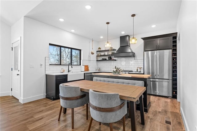 kitchen with light wood-type flooring, a sink, appliances with stainless steel finishes, decorative backsplash, and custom exhaust hood