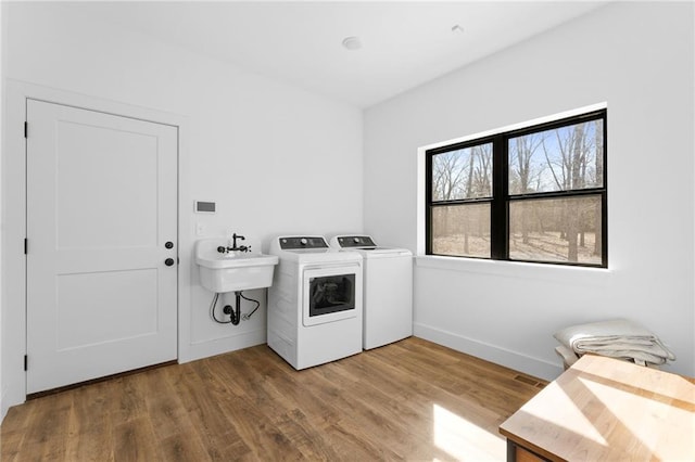 laundry area featuring baseboards, laundry area, separate washer and dryer, wood finished floors, and a sink