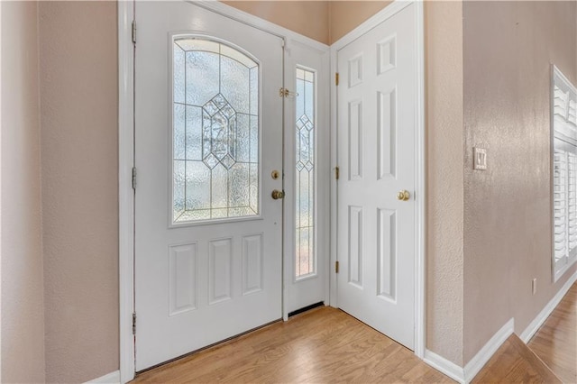 foyer entrance with a textured wall, baseboards, and light wood finished floors