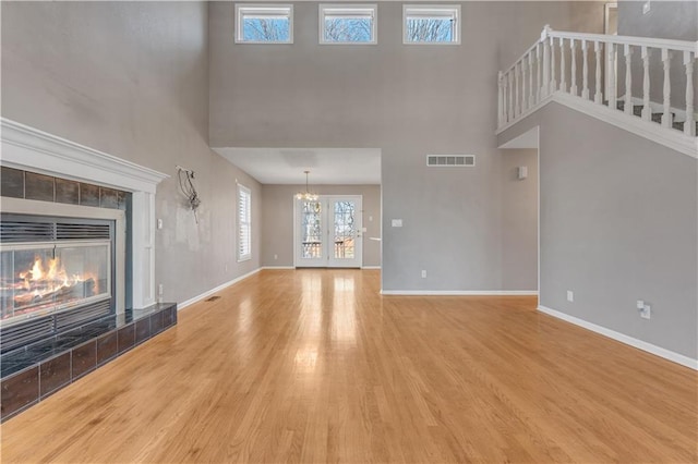 unfurnished living room featuring visible vents, a tiled fireplace, wood finished floors, baseboards, and a chandelier