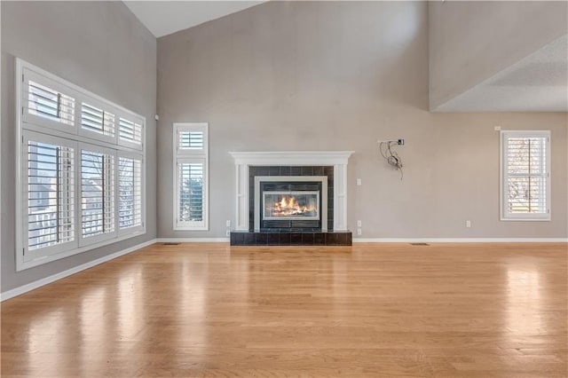 unfurnished living room featuring plenty of natural light, light wood-style floors, and a towering ceiling