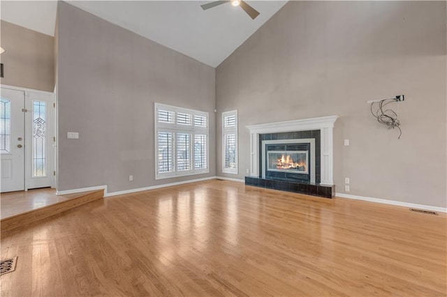 unfurnished living room featuring wood finished floors, baseboards, high vaulted ceiling, ceiling fan, and a tile fireplace