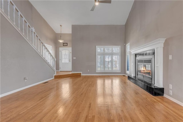 unfurnished living room featuring baseboards, stairs, a fireplace, light wood-style floors, and a towering ceiling