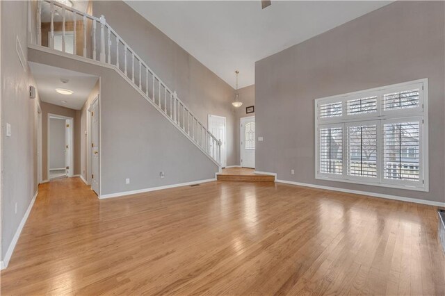 unfurnished living room featuring stairs, a high ceiling, wood finished floors, and baseboards