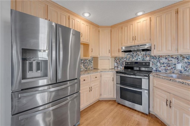 kitchen featuring tasteful backsplash, light stone countertops, under cabinet range hood, appliances with stainless steel finishes, and light wood-style floors