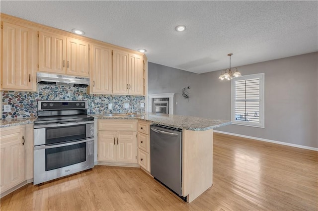 kitchen with light wood finished floors, a peninsula, a sink, under cabinet range hood, and appliances with stainless steel finishes