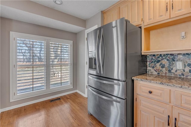 kitchen with light stone counters, baseboards, light wood finished floors, stainless steel refrigerator with ice dispenser, and backsplash