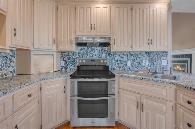 kitchen featuring under cabinet range hood, a sink, tasteful backsplash, range with two ovens, and light stone countertops