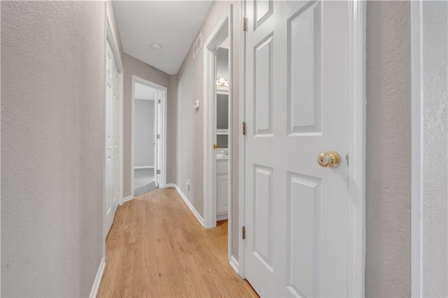 hallway with visible vents, light wood-style flooring, baseboards, and a textured wall