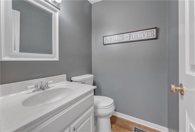 bathroom with baseboards, toilet, wood finished floors, and vanity