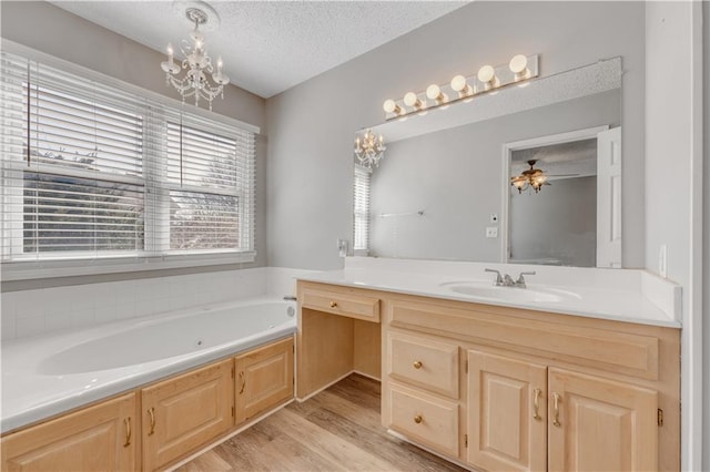 bathroom with vanity, wood finished floors, an inviting chandelier, a textured ceiling, and a garden tub