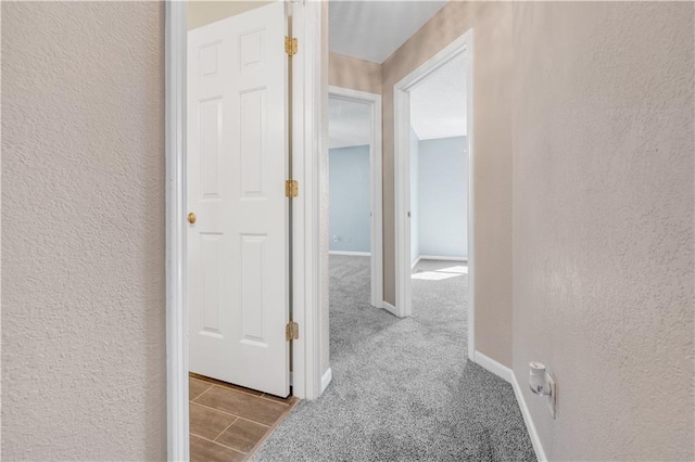 hallway featuring baseboards, carpet, and a textured wall